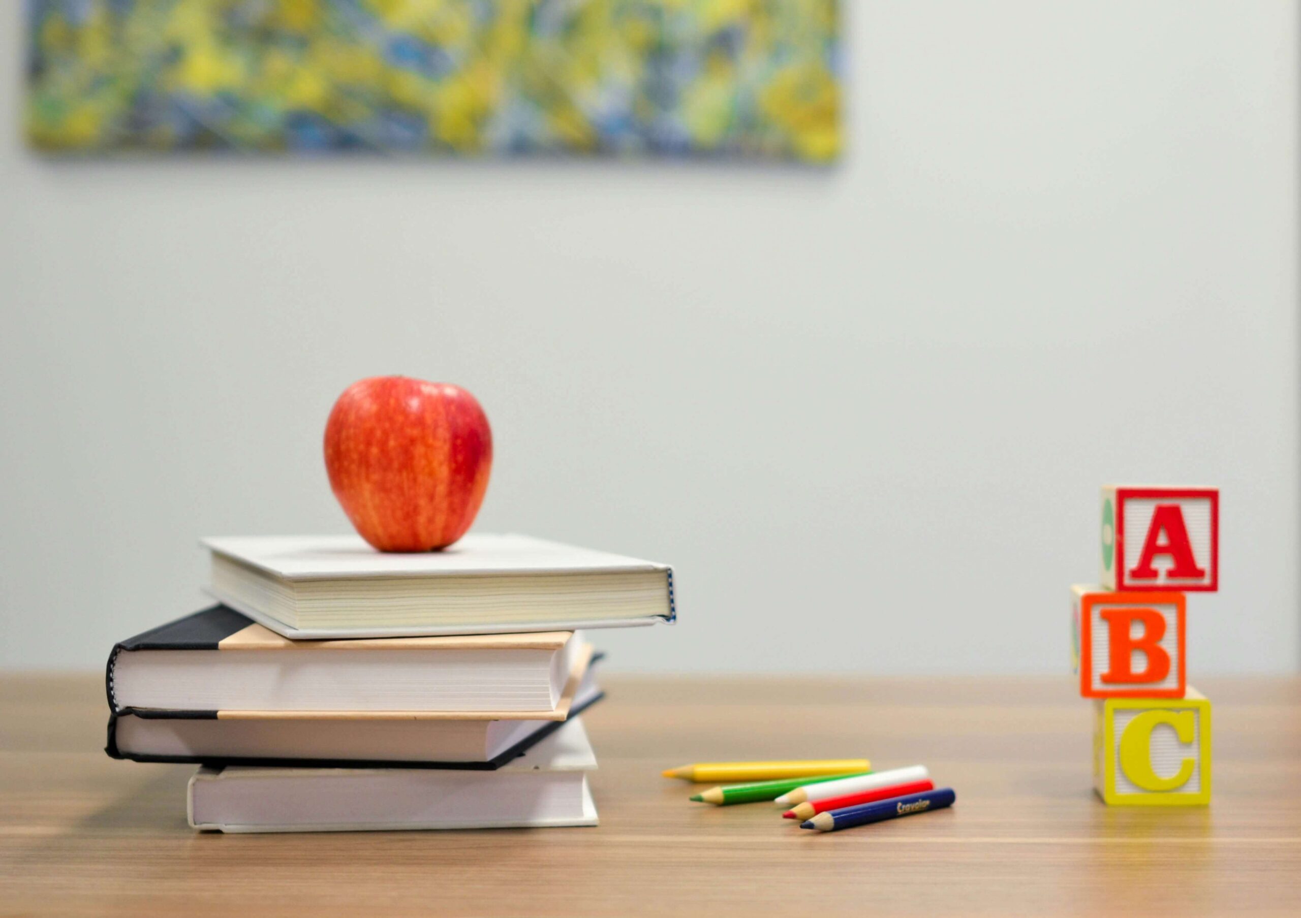 pile of books with apple on top to the left and block letters ABC to the right all sitting on a desk