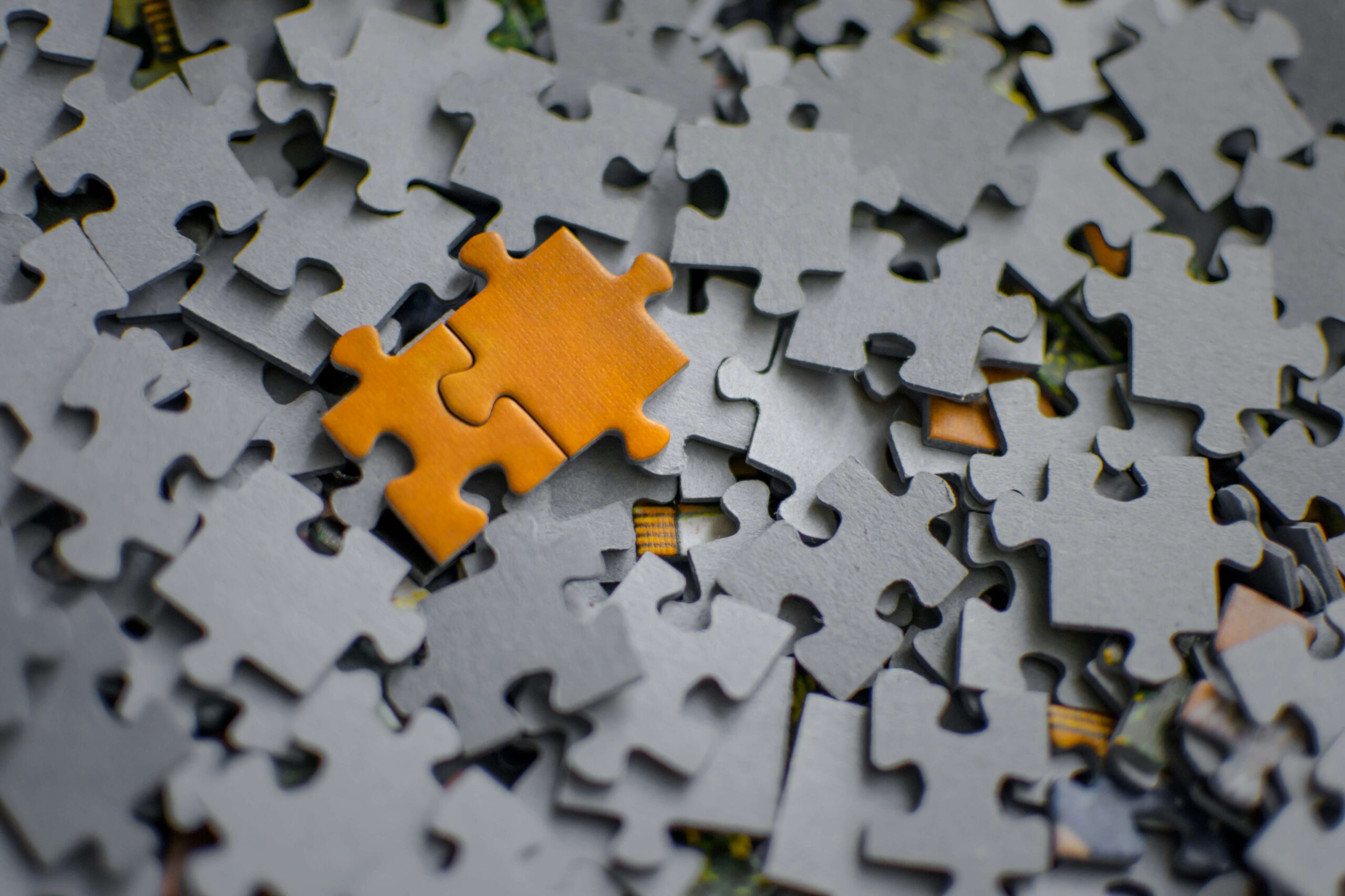 jigsaw pieces with 2 orange pieces fitting together on top of a pile of grey ones