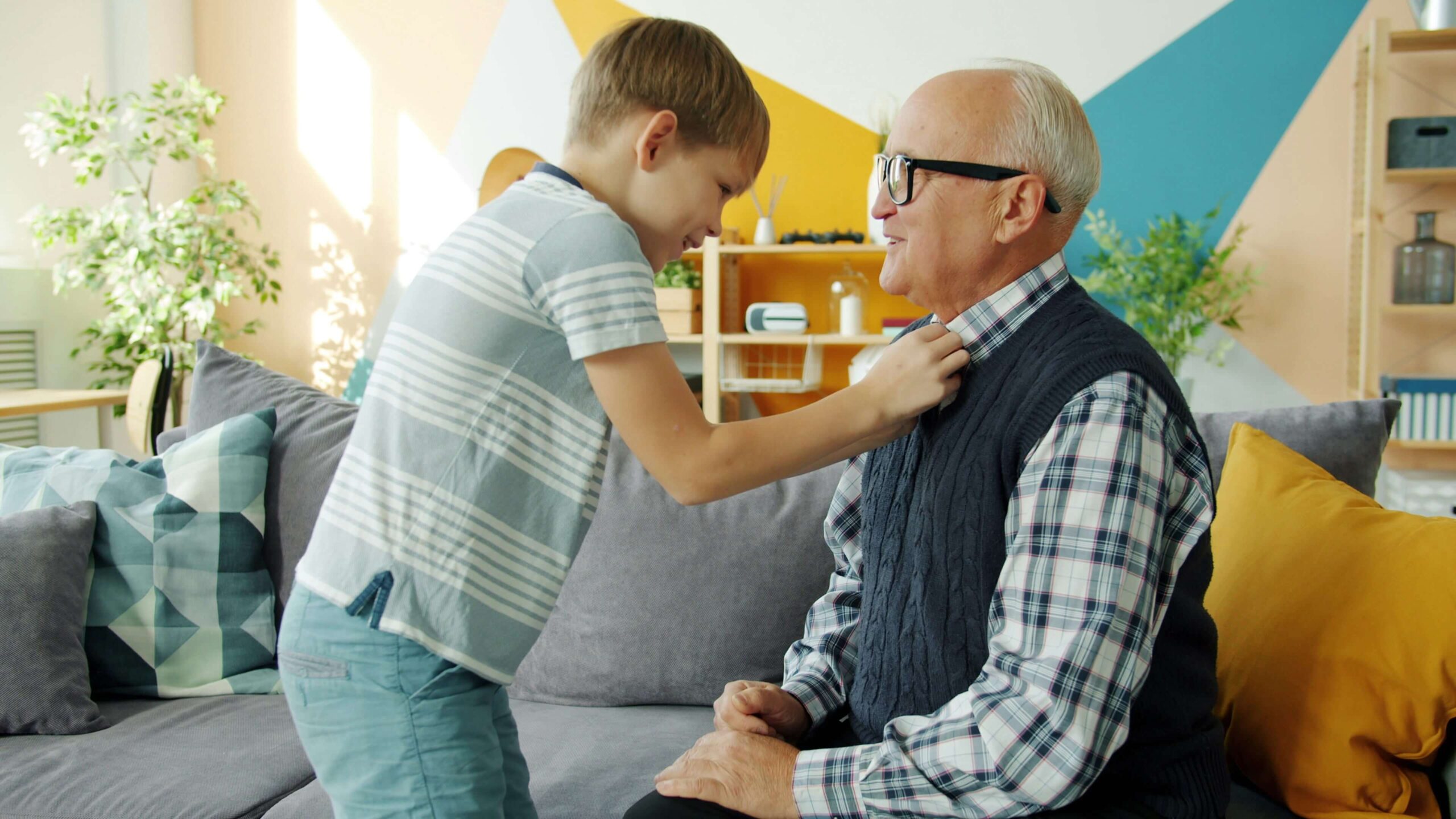 young child fixing older males collar while he sits on the sofa