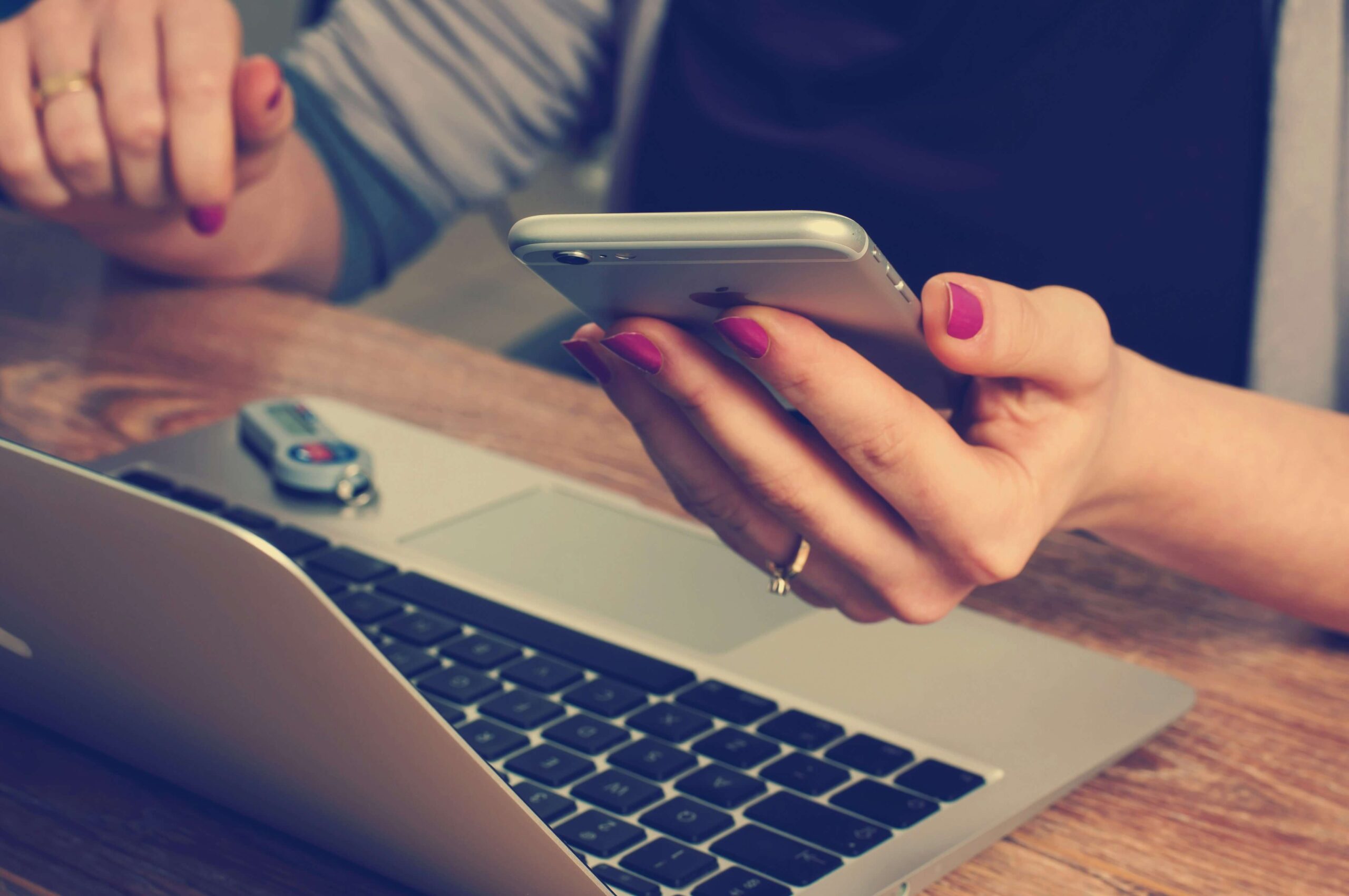 female hand holding mobile phone over a laptop keyboard